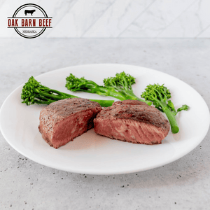 Medium rare steak cut in half with broccoli on a plate with white background and an Oak Barn Beef  logo in the corner