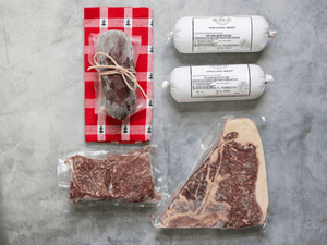 Meat displayed on a grey background. there is also a red napkin under a summer sausage package.
