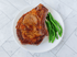 Large, Bone In Beef Ribeye on a white plate with green vegetables next to it.