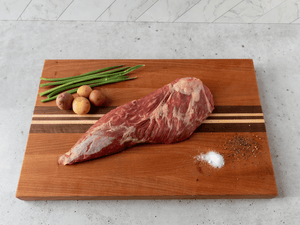 Tri Tip beef Roast raw and on a cutting board with a white background. Potatoes and Green Beans next to it on the cutting board