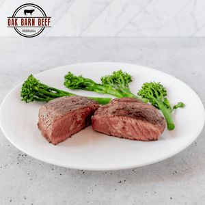 Medium rare steak cut in half with broccoli on a plate with white background and an Oak Barn Beef  logo in the corner