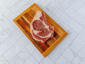 Large, Bone In Beef Ribeye, not cooked, on a cutting board.